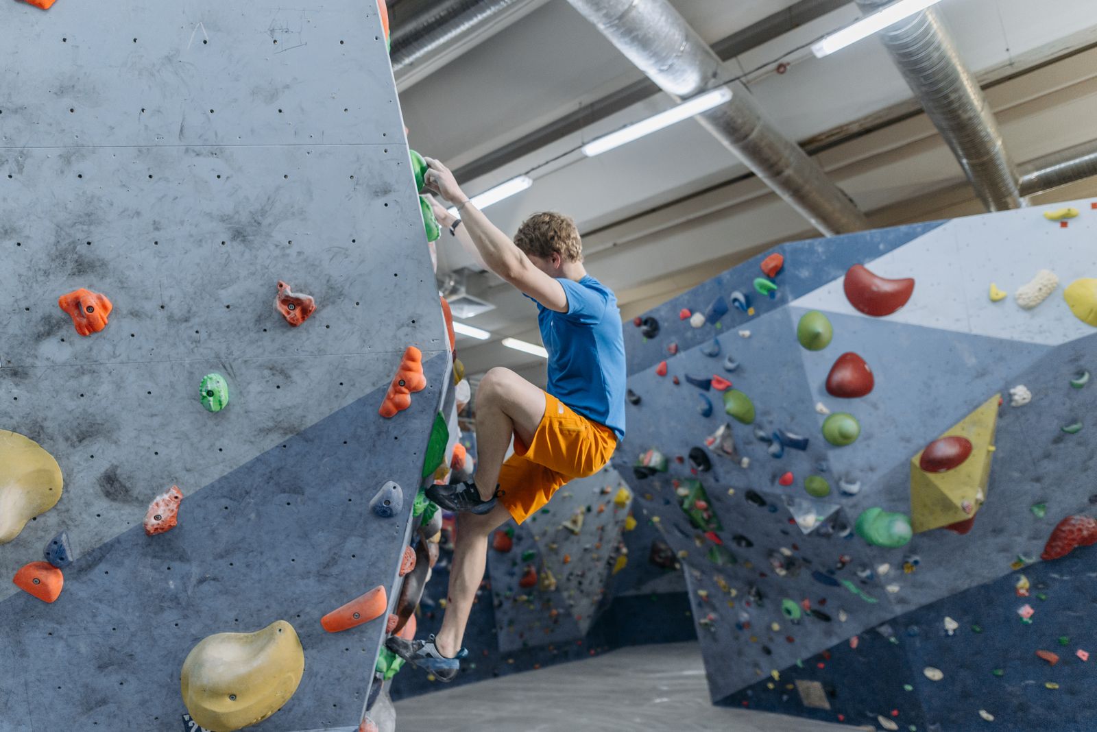 A climber in a blue shirt bouldering on an indoor wall